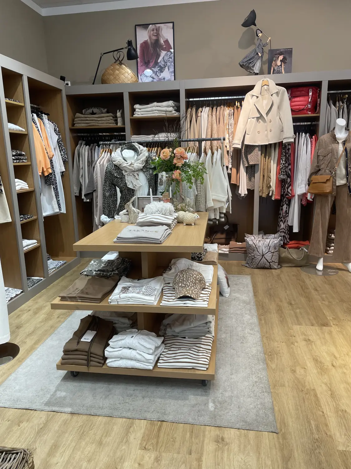 Abig-Moden - Modeboutique - Ein gut beleuchtetes Bekleidungsgeschäft mit ordentlich aufgereihten Kleiderständern in neutralen Farbtönen und einem zentralen, mehrstufigen Holzdisplay.