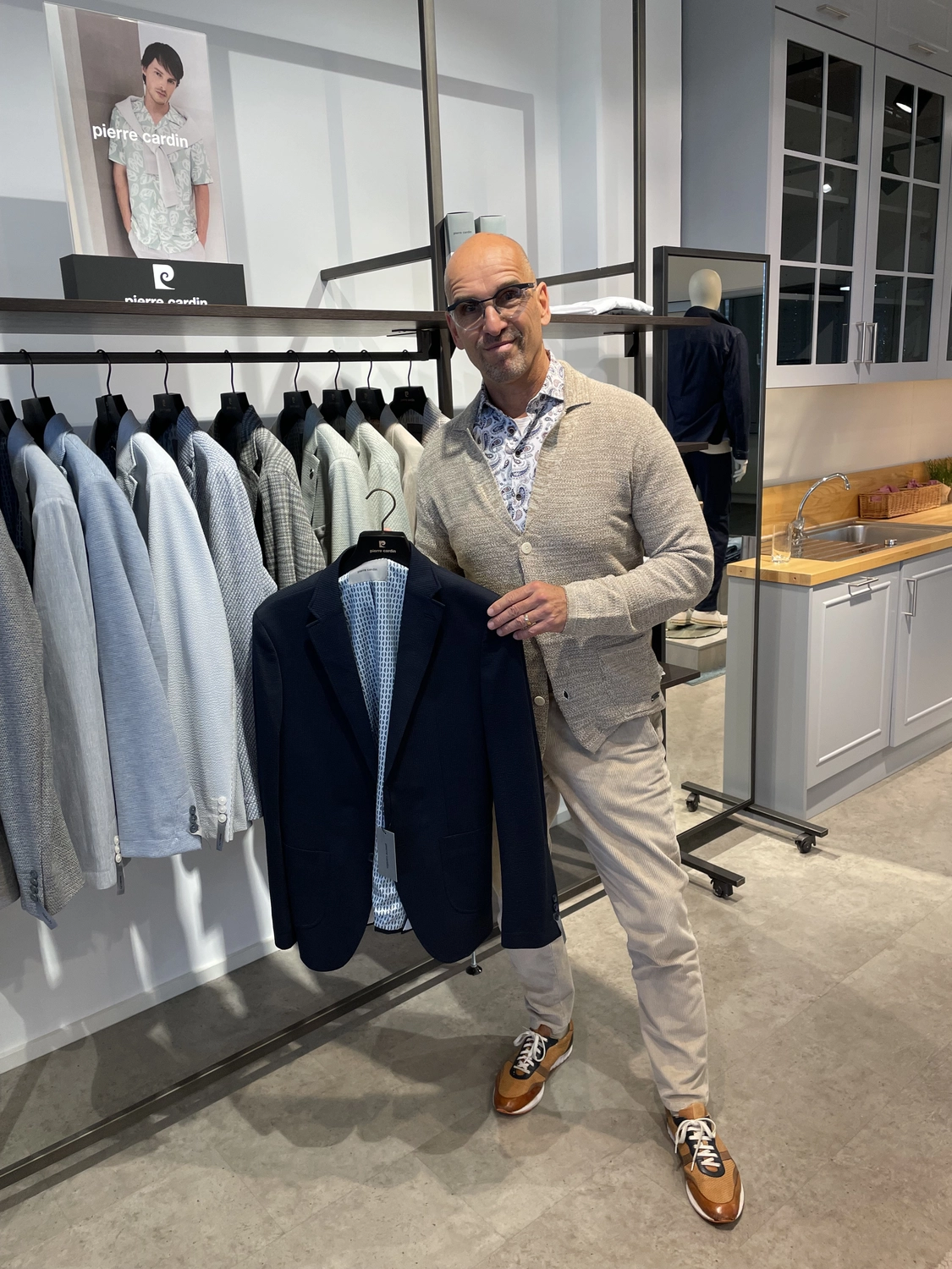 Abig-Moden - Modeboutique - Ein Mann mit Sonnenbrille lächelt und hält in einem Bekleidungsgeschäft ein hellgrünes Poloshirt in der Hand.