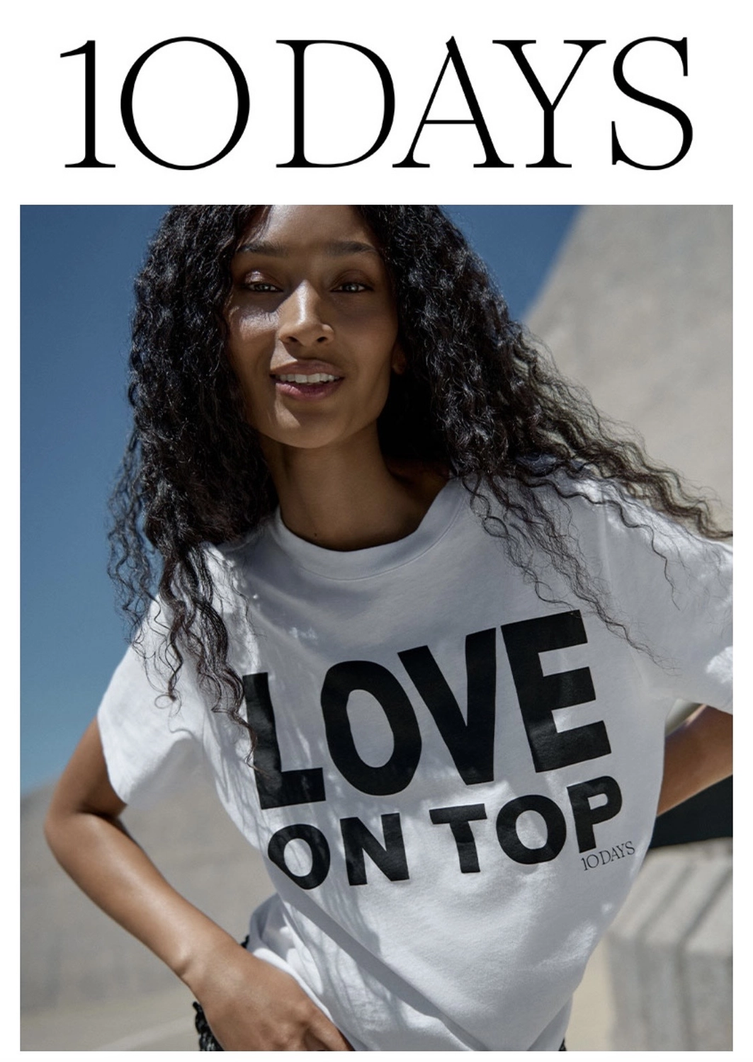 Abig-Moden - Modeboutique - Ein Model mit langen, lockigen Haaren posiert in einem weißen T-Shirt mit dem fettgedruckten schwarzen Schriftzug „LOVE ON TOP“ unter der Überschrift „10 DAYS“.