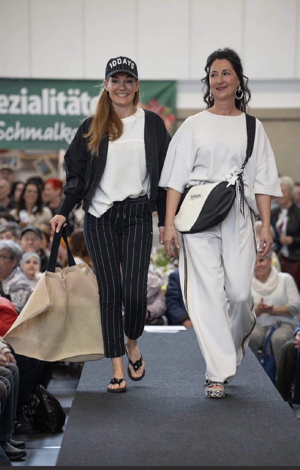 Abig-Moden - Modeboutique - Eine Frau lächelt aus dem Schaufenster einer Ilse Jacobsen Boutique, das von roten Backsteinen umrahmt und mit fünf kleinen lila Topfpflanzen auf dem Fenstersims dekoriert ist.